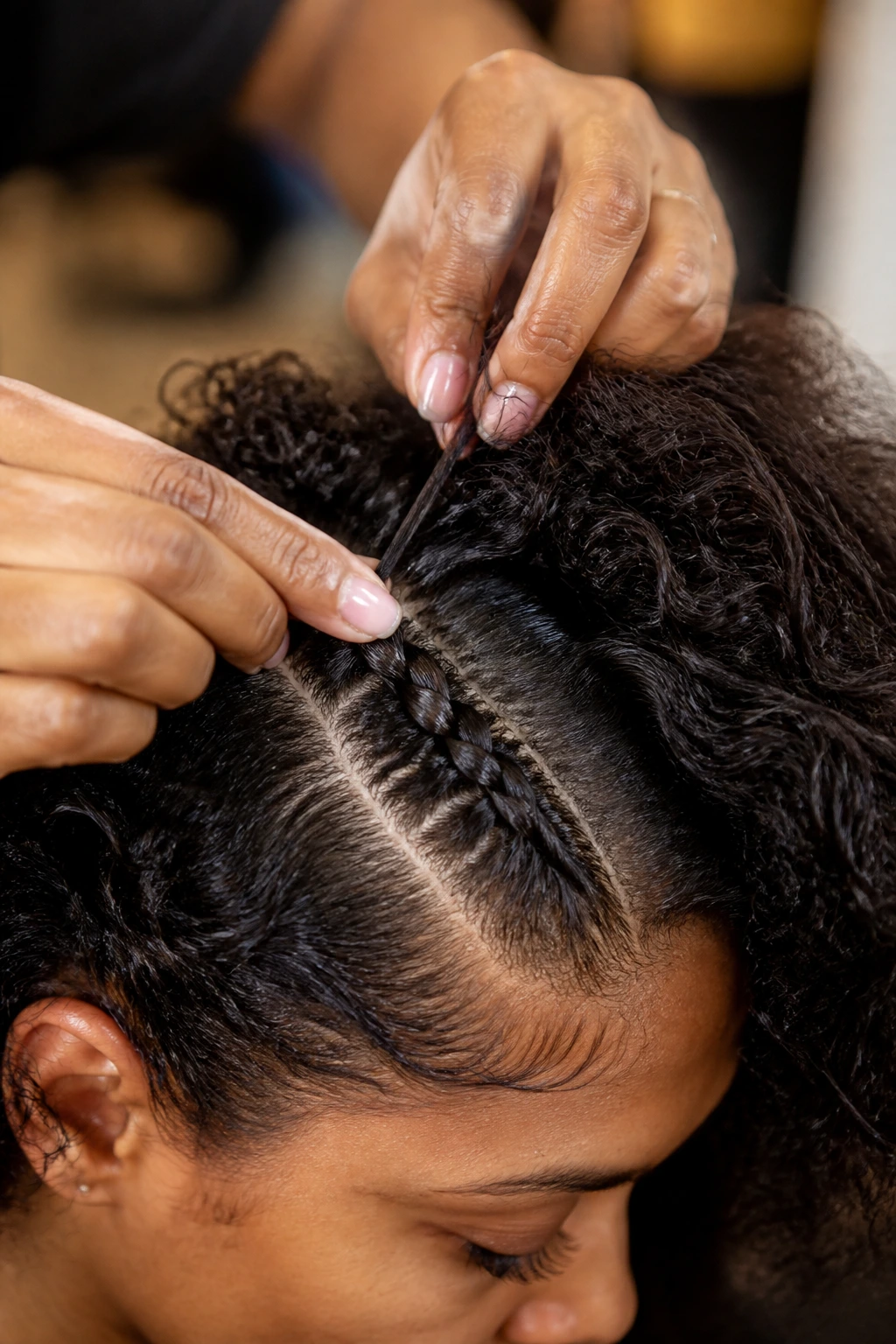 Close-up of hands applying steady tension while braiding curly hair