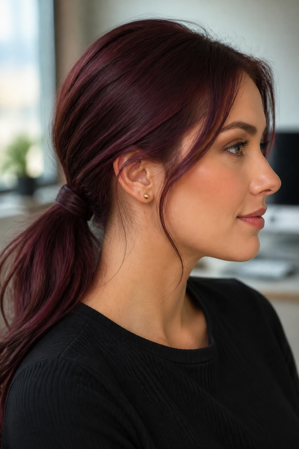 Close-up of a real woman with a textured deep burgundy low ponytail at the nape in an office setting