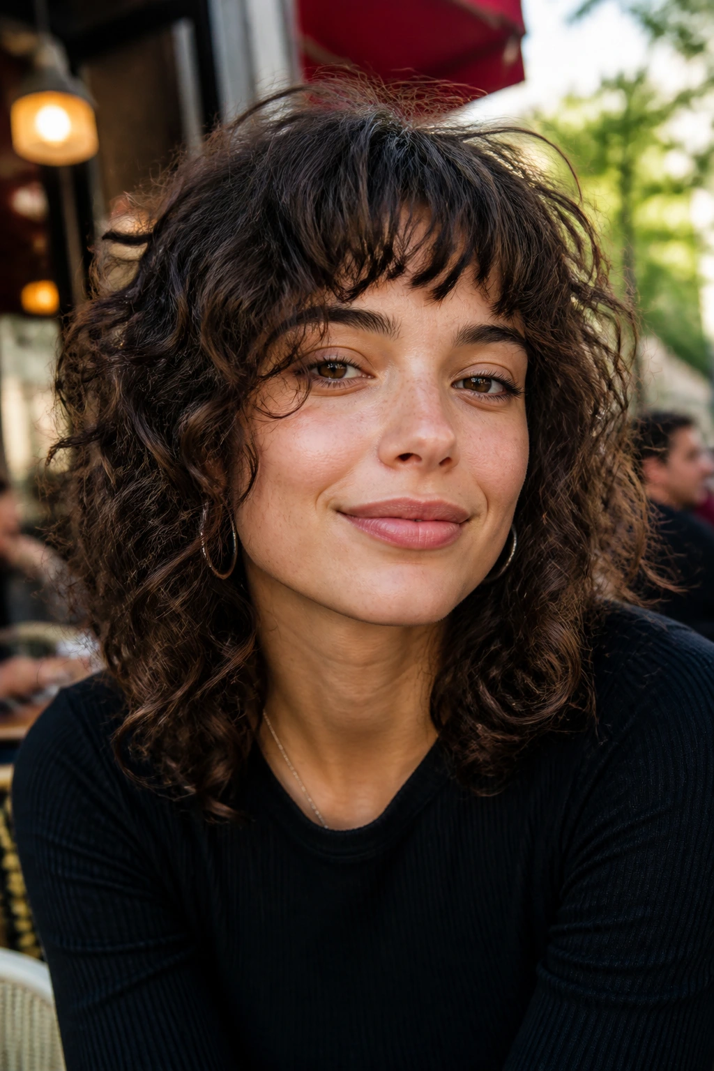 Close-up of a woman with choppy bangs and tousled curls in soft daylight.