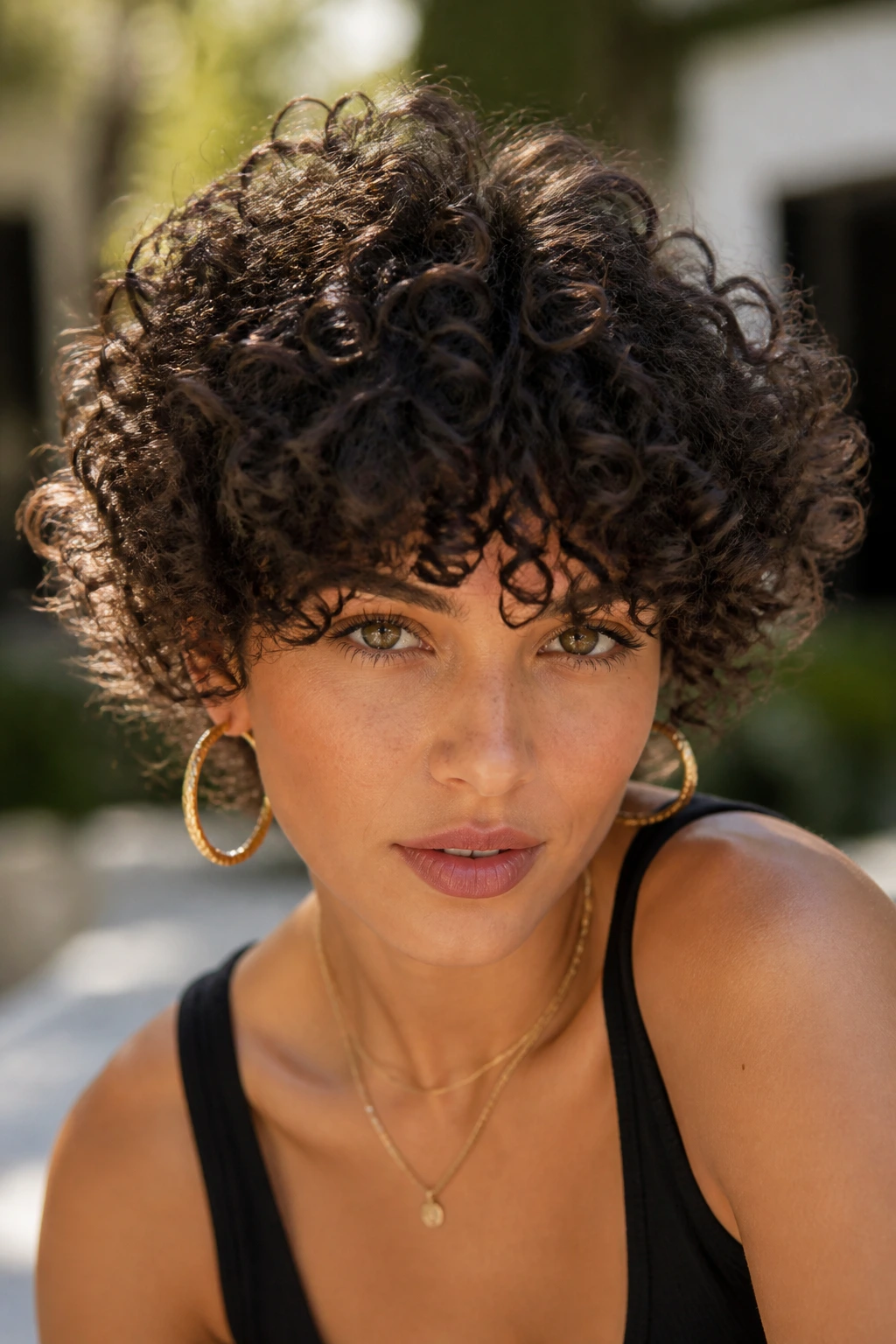 Close-up of a woman with dense crown-cut curly fringe in bright courtyard light