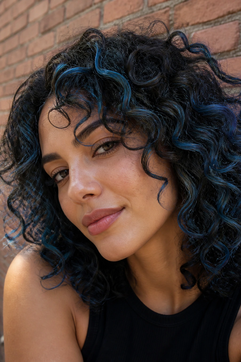 Close-up of real person with denim blue streaks in curly hair against brick wall