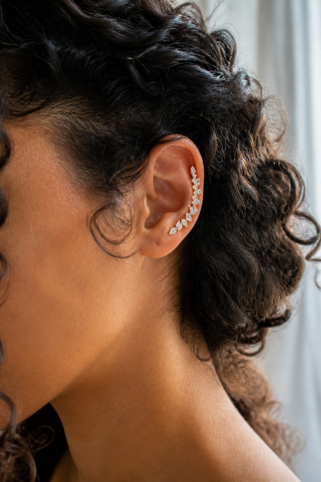 Close-up of a real person's ear with a cascading diamond climber cuff along the ear