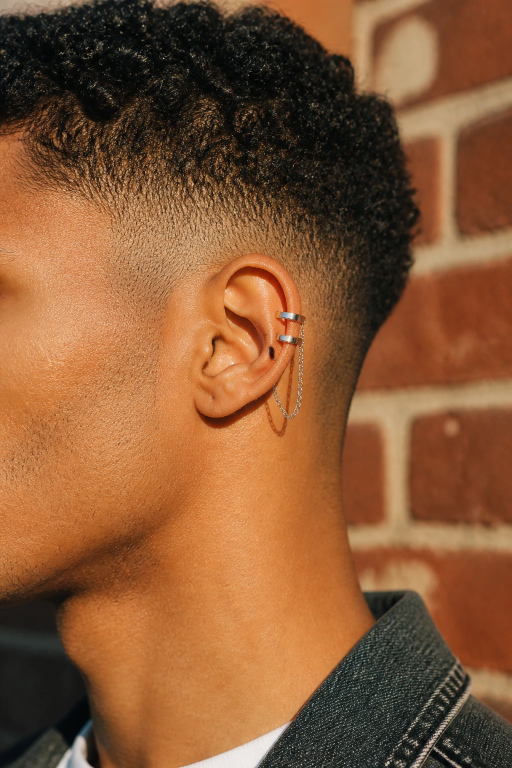 Close-up of ear with industrial double-band cuff and chain on a real person with short curly hair