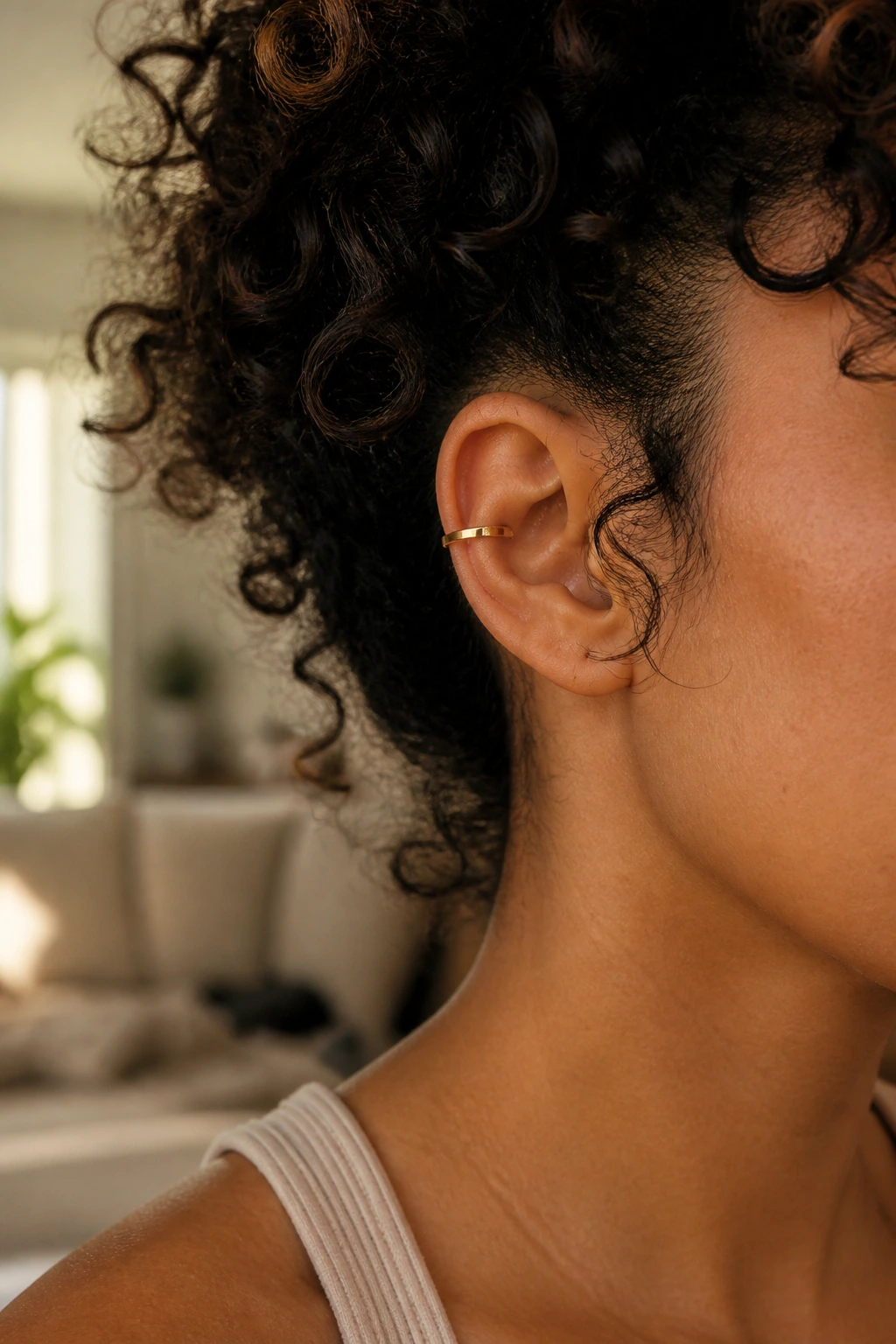 Close-up of a real woman's ear wearing a gold minimalist ear cuff on the helix with curly hair framing