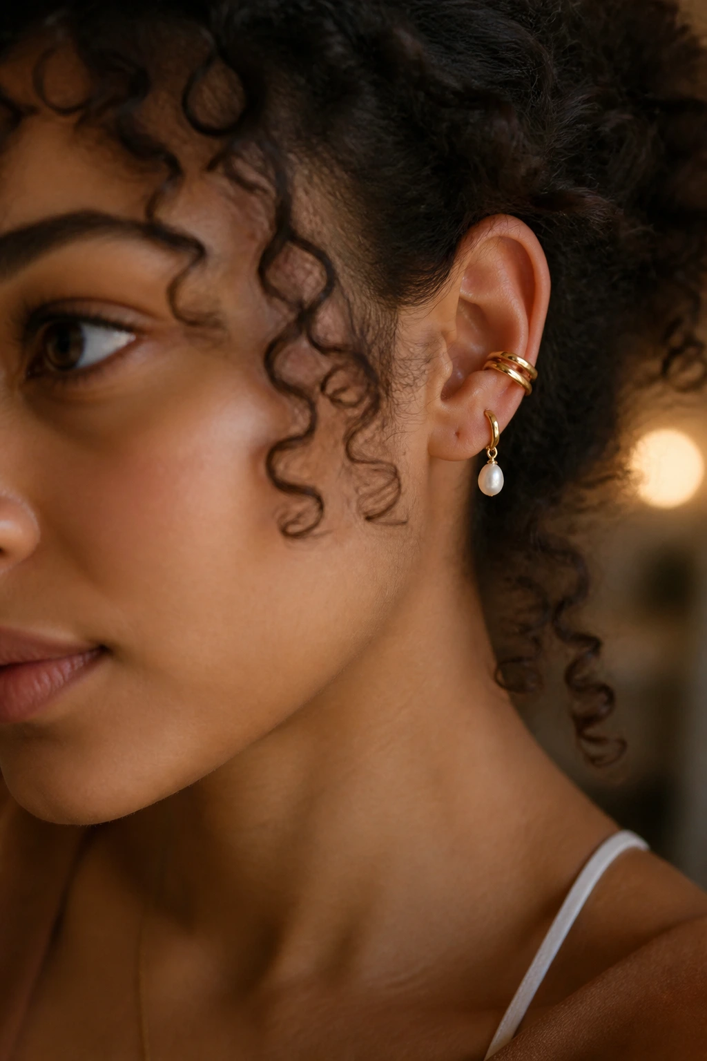 Close-up of ear with pearl-dangling cuff on curly hair in warm light