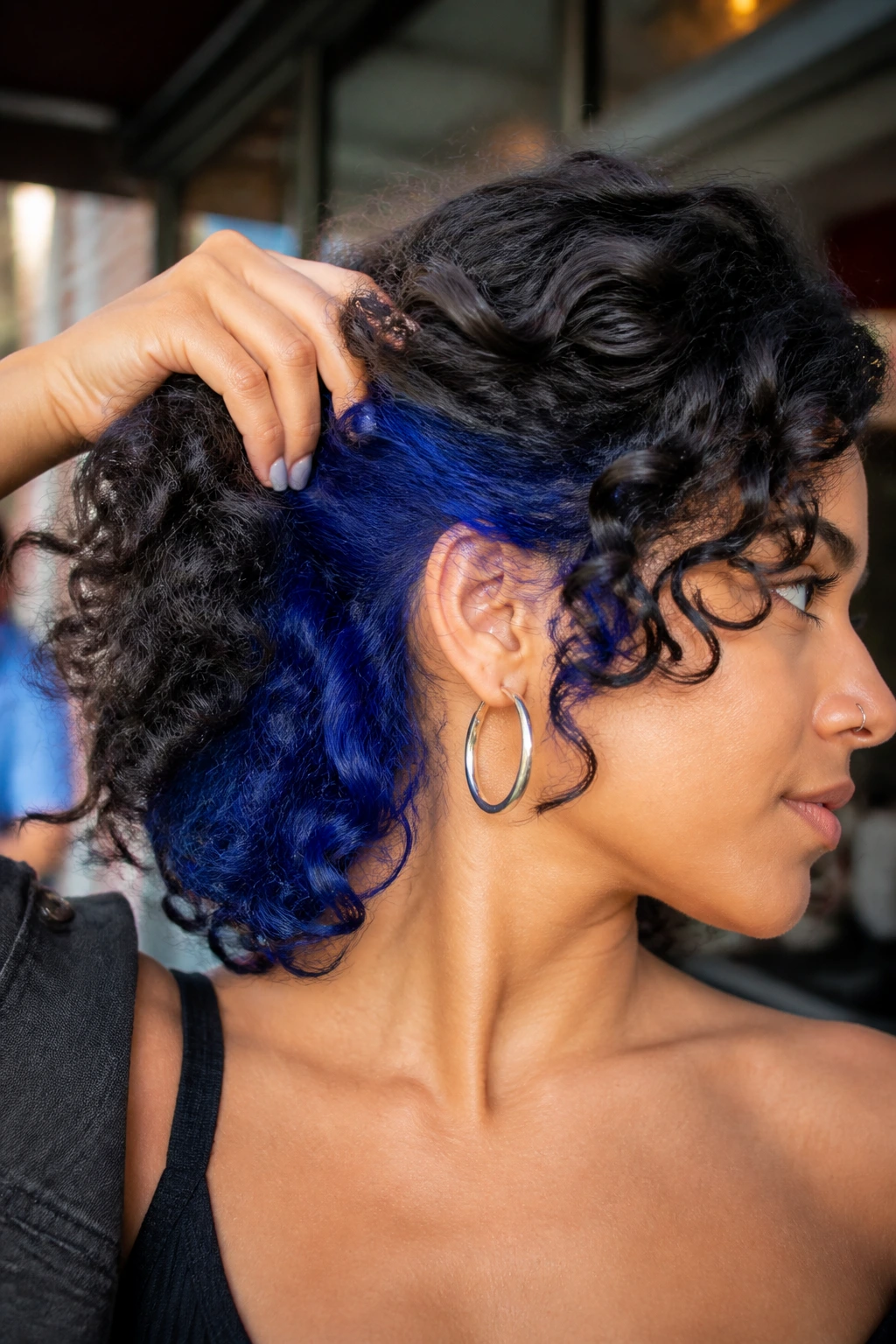 Close-up of a real woman with dark curly hair showing electric cobalt peekaboo underlayer peeking from beneath curls.