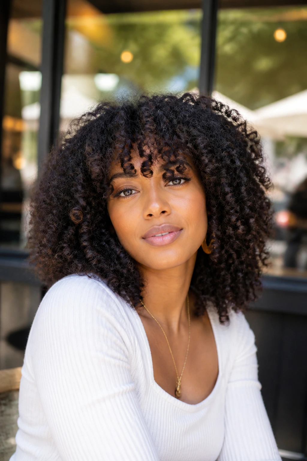 Medium close-up of a real person with feathery kinky curly fringe in sunny cafe setting
