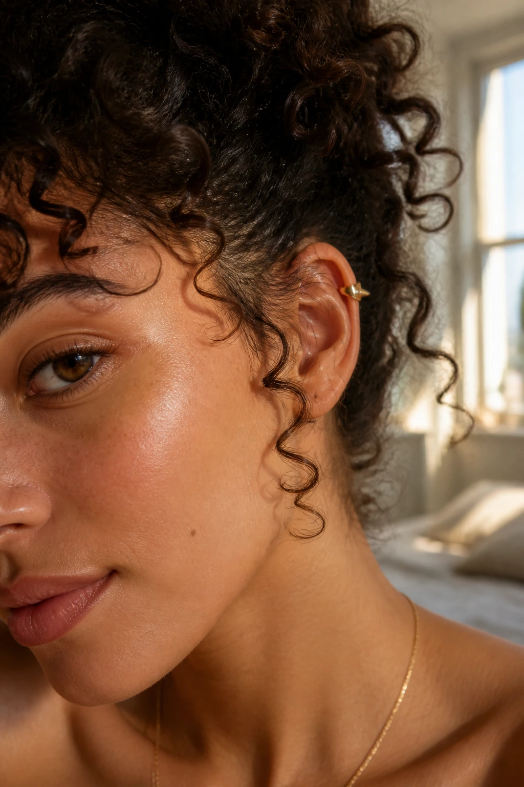Close-up of ear with geometric spike cuff on curly hair, warm window light