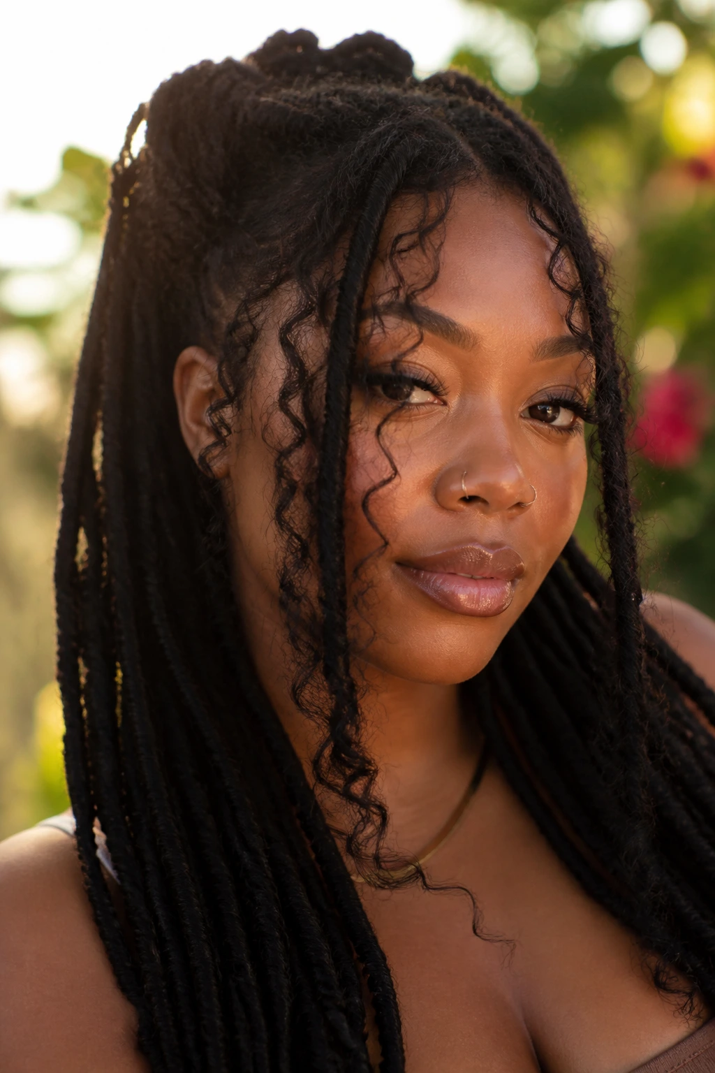 Portrait of a woman with goddess locs and tendrils framing the face in sunlit garden