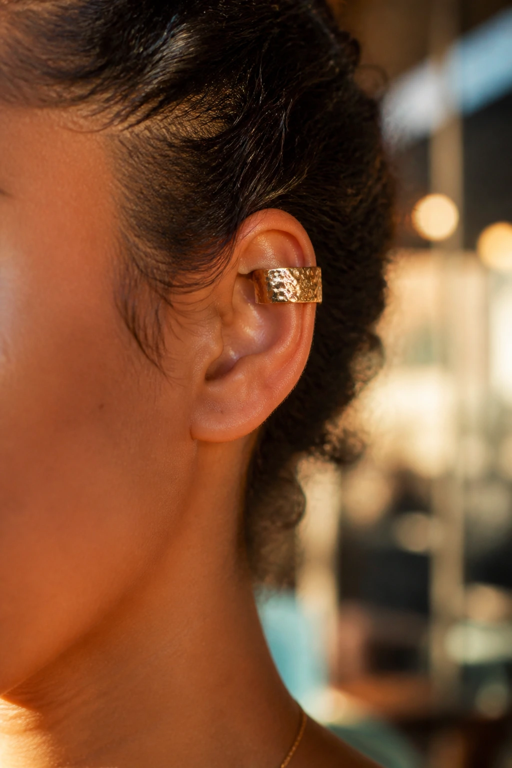 Close-up of ear with hammered metal cuff and pulled-back curls in golden hour light