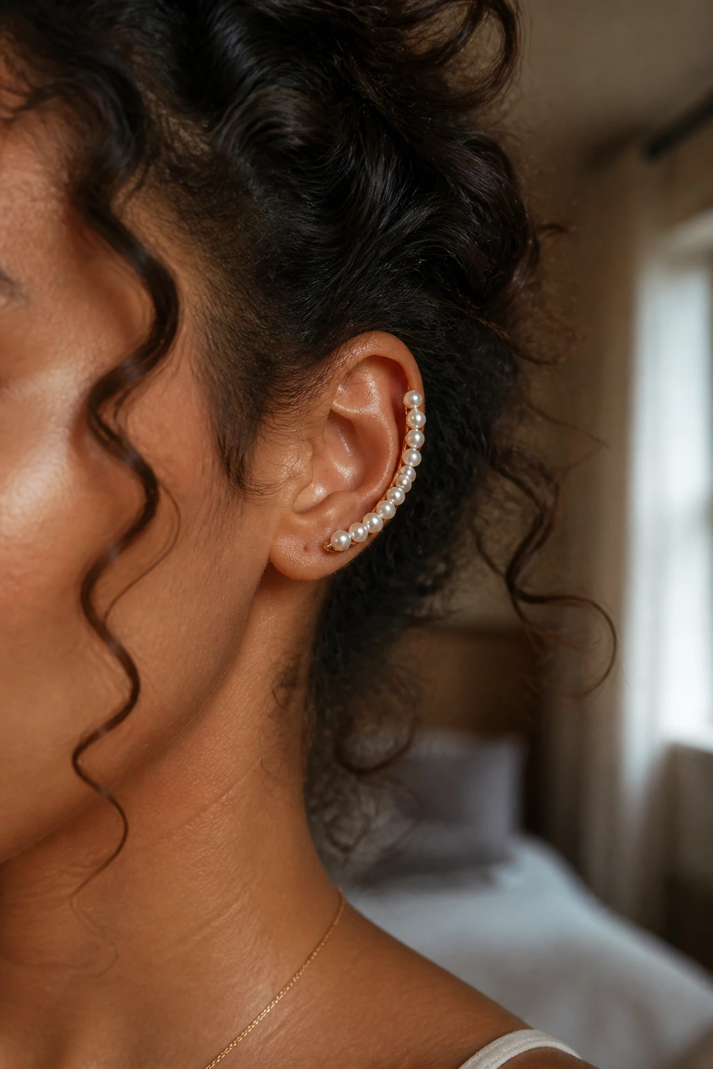 Close-up of a woman's ear with a pearl-embellished ear cuff amid curly hair