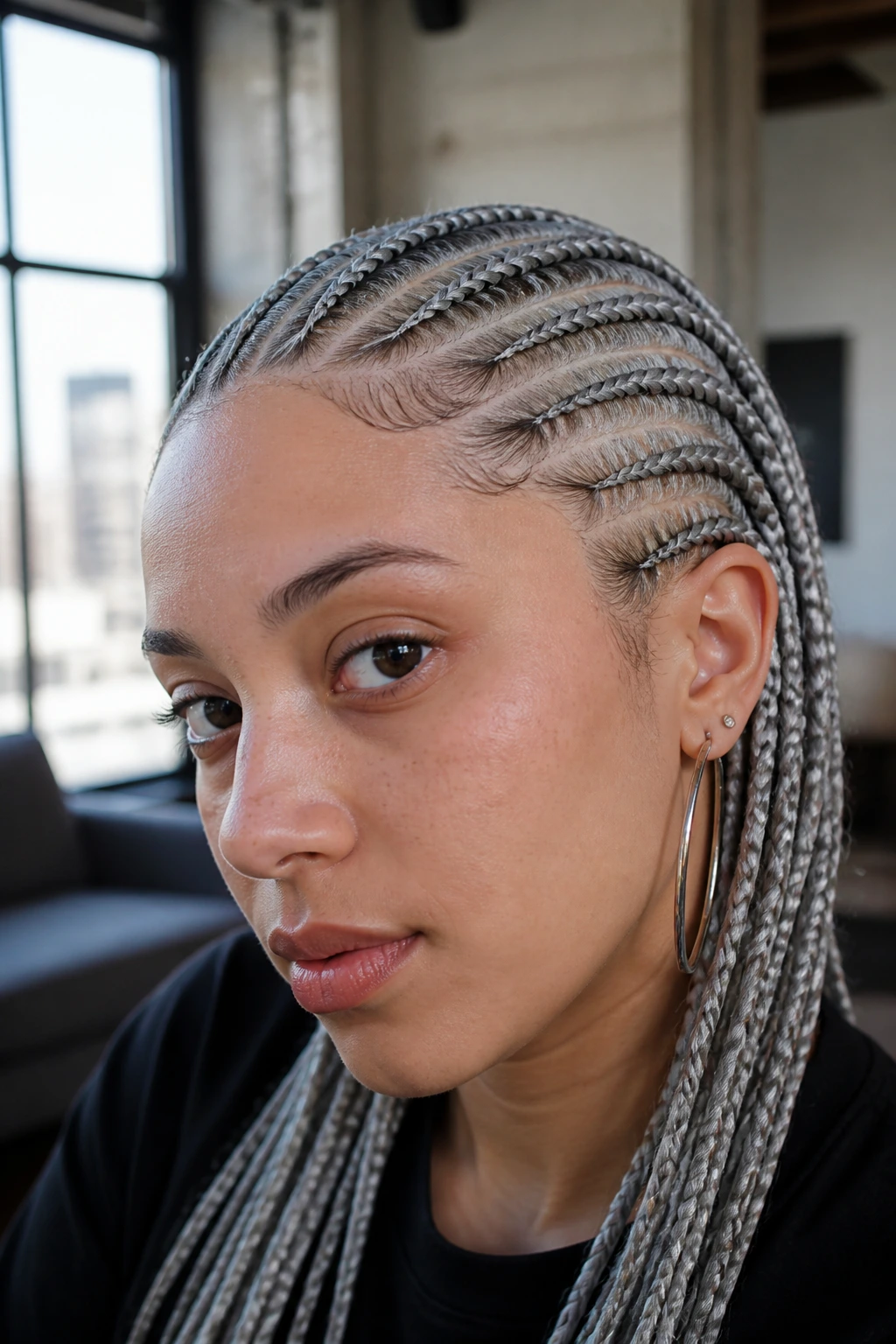 Close-up portrait of a person with silver-gray braids in a modern loft setting.