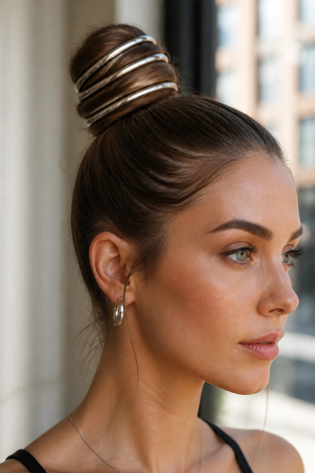 Close-up of a sleek bun with metallic hair rings on a real person
