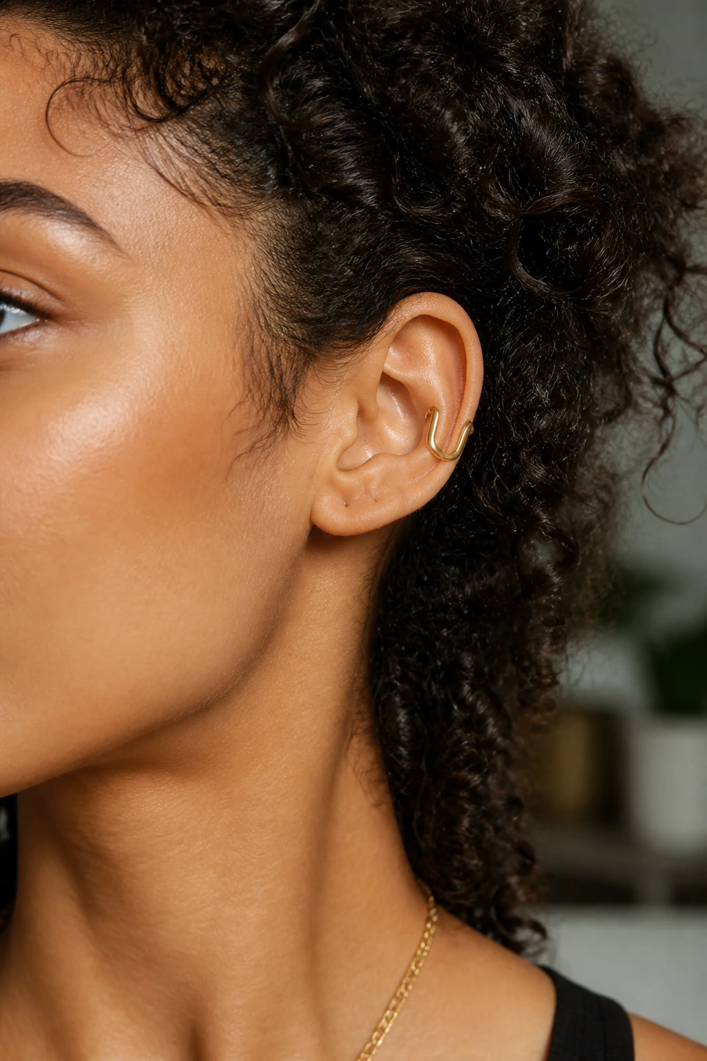 Close-up of ear with sleek U-shaped cuff on curly hair in soft daylight