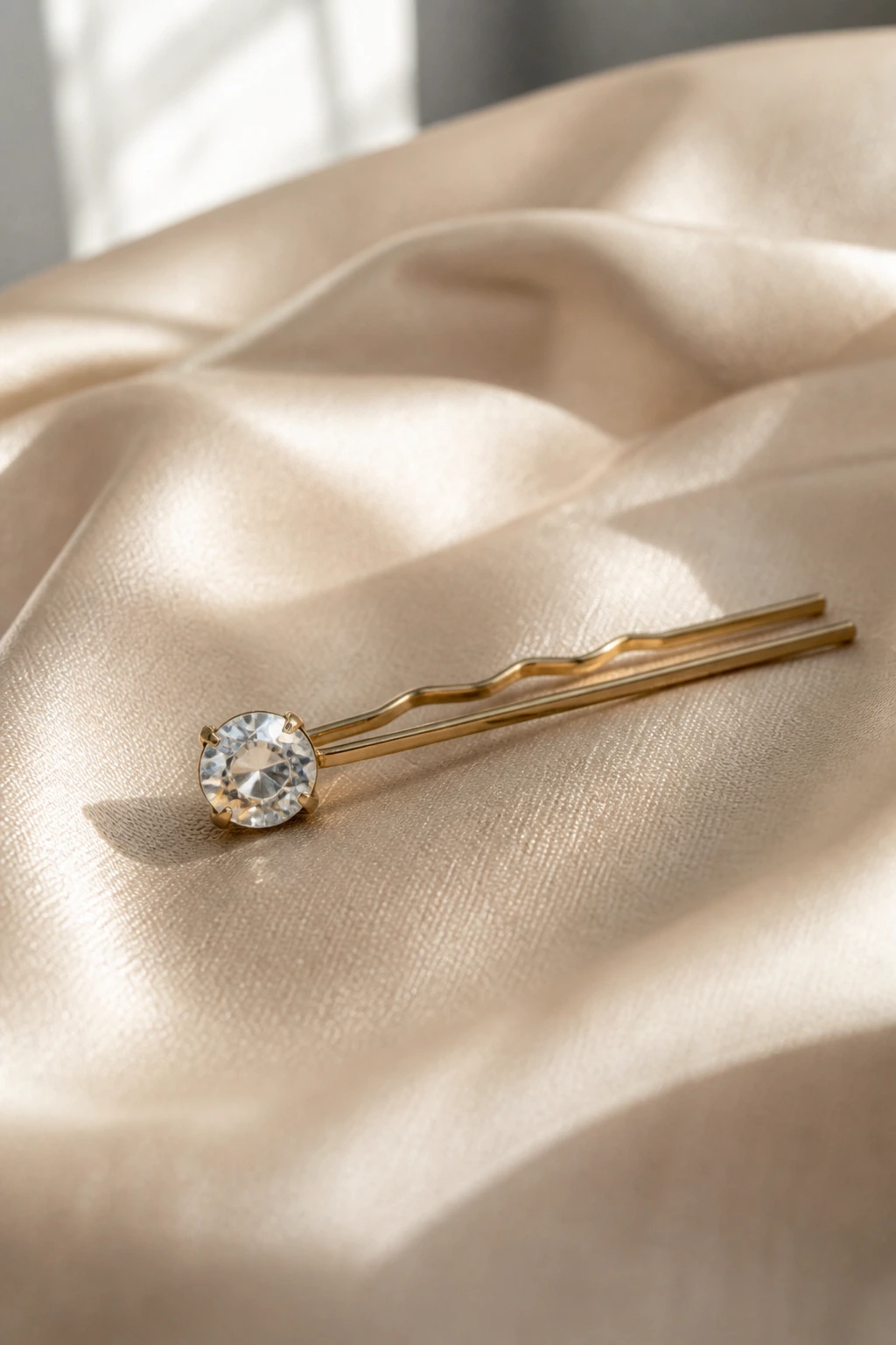 Close-up of a crystal-tipped hairpin resting on satin fabric with soft light