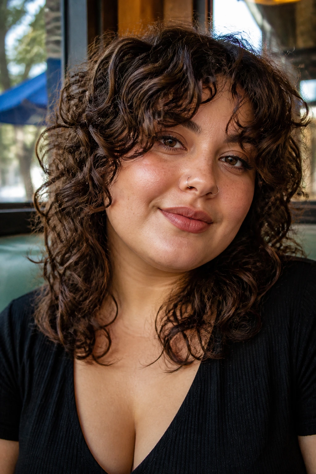 Close-up portrait of a real woman with curly shag and curtain bangs in daylight at a cafe