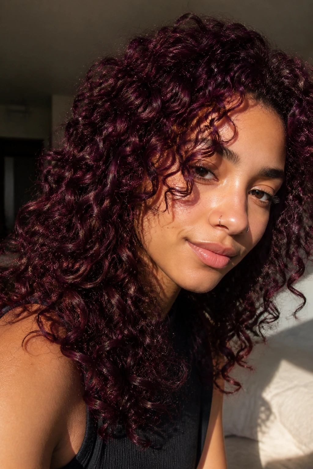 Close-up of a real person's curls in deep plum and burgundy tones catching sunlight