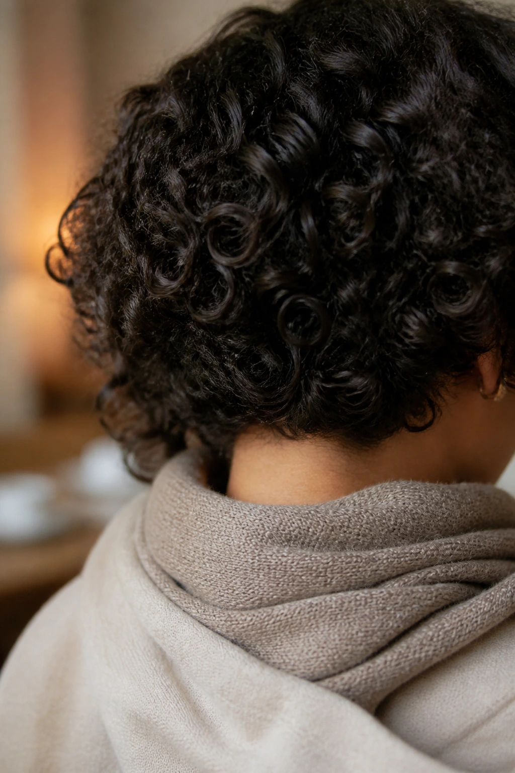 Real person wearing a curly 20-inch wig with hair tucked away from a wool scarf in a winter home setting.